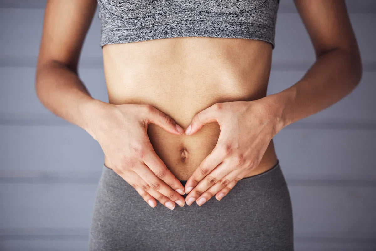 Frau in Sportkleidung formt mit ihren Händen ein Herz über dem Bauch – Symbol für Darmgesundheit und Wohlbefinden.