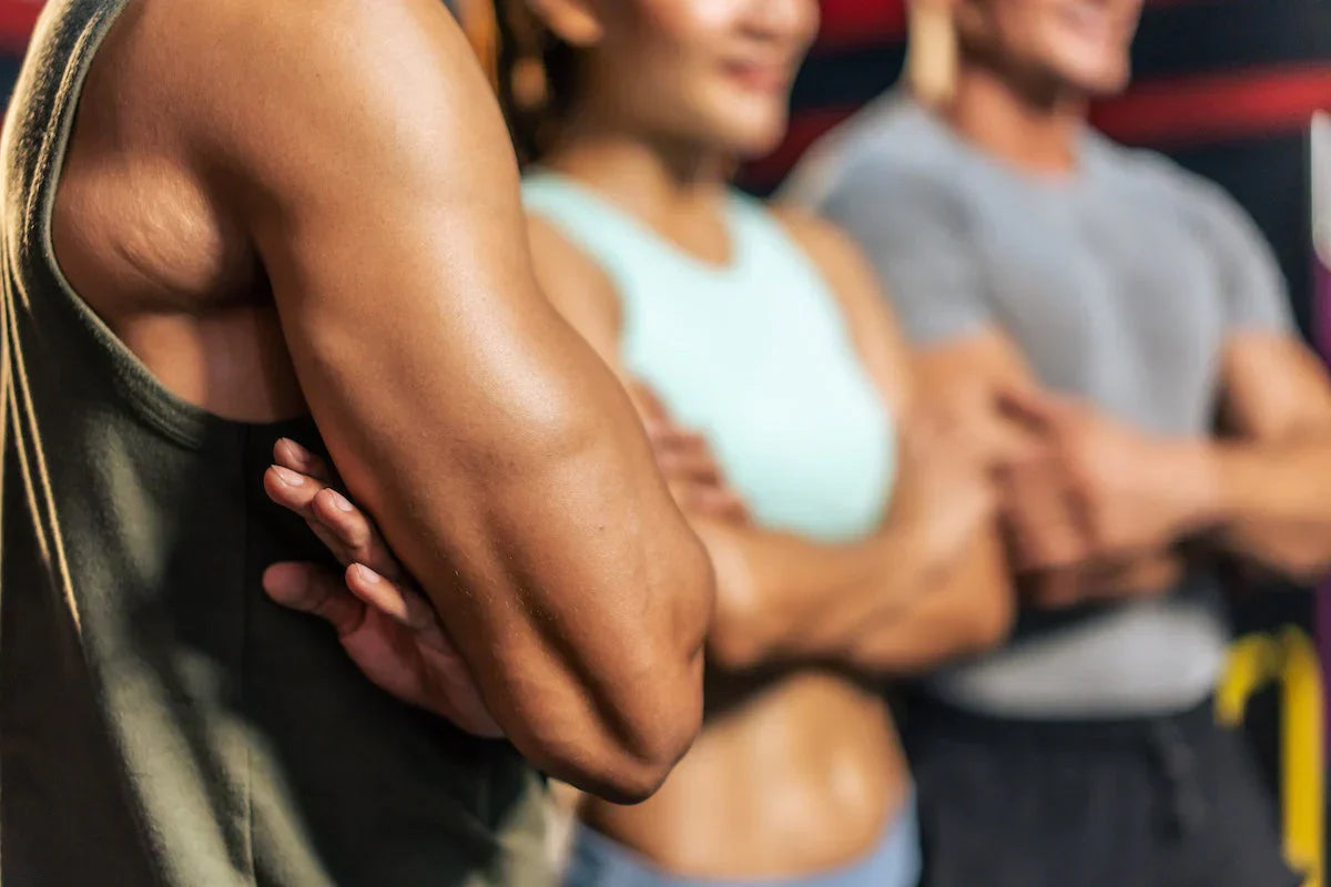 Drei sportliche Personen mit verschränkten Armen in Trainingskleidung – Fokus auf muskulöse Oberarme und aktive Körperhaltung.