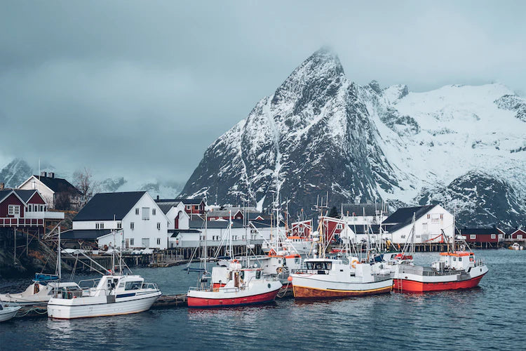 Fischerboote im Hafen des verschneiten Fischerdorfs Hamnøy auf den Lofoten-Inseln in Norwegen, mit dramatischer Bergkulisse und winterlicher Atmosphäre.